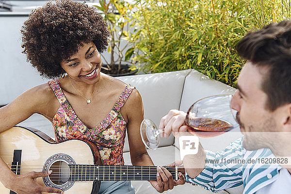 Glückliche Frau spielt Gitarre für Mann trinkt Rotwein auf Penthouse-Terrasse
