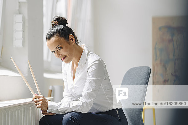 Weibliche Fachkraft  die Schlagzeugstöcke hält  sitzt auf einem Stuhl im Büro zu Hause