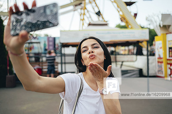 Young woman blowing kiss while taking selfie in amusement park