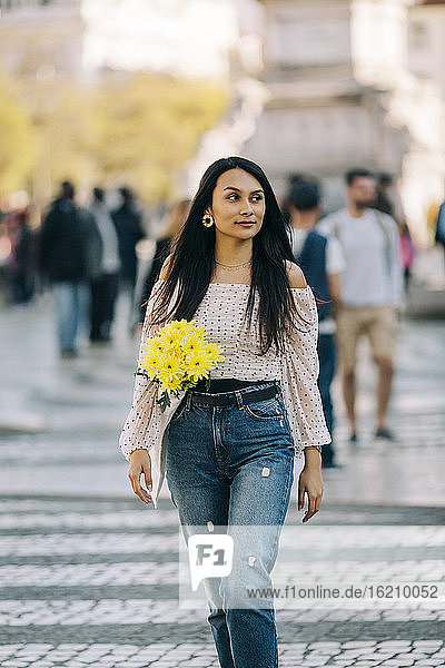 Young woman with bouquet walking on street in city