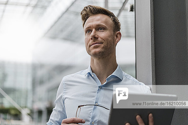 Confident businessman with digital tablet looking away in city