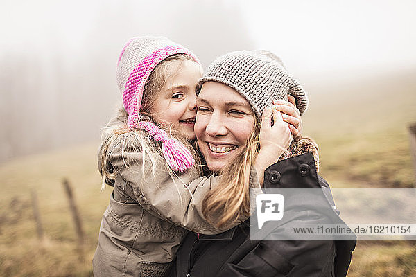Mutter und Tochter umarmen und lachen in einer nebligen Landschaft