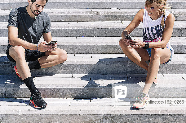 Couple using smart phones while sitting on steps in city during sunny day