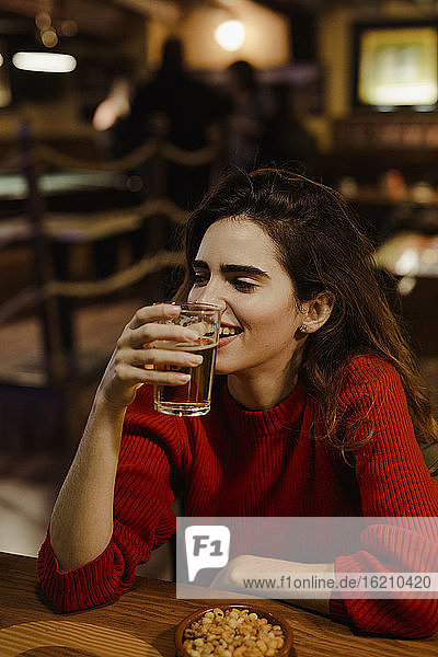 Nahaufnahme einer lächelnden Frau  die ein Bierglas in der Hand hält  während sie an einem Tisch im Restaurant sitzt