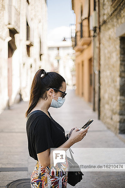 Frau trägt Schutzbrille und benutzt Smartphone in Gasse