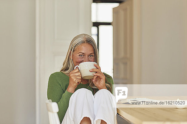 Smiling woman drinking coffee by table at home