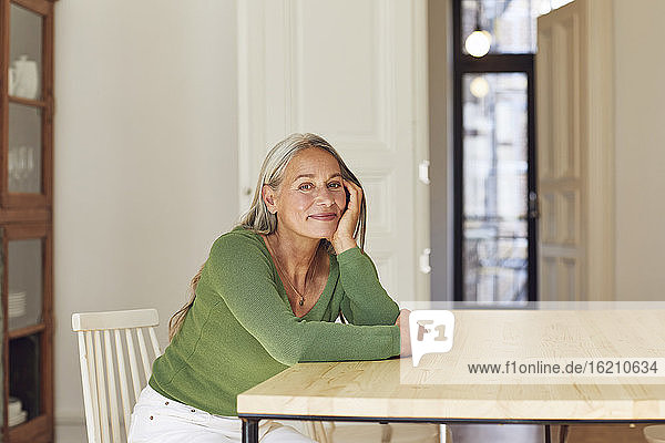 Lächelnde reife Frau träumt am Tisch zu Hause