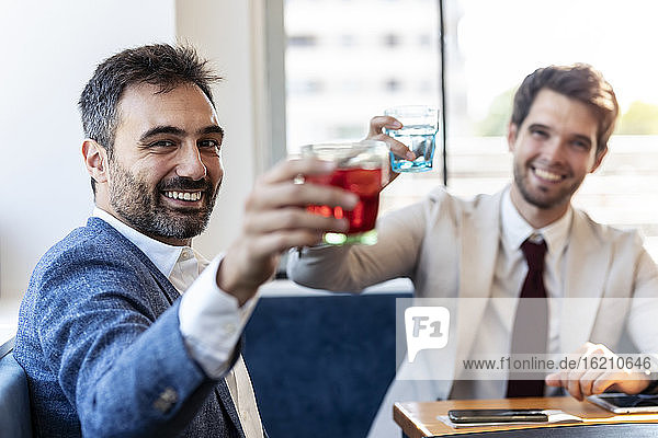 Happy businessmen cheering while having drinks at cafe