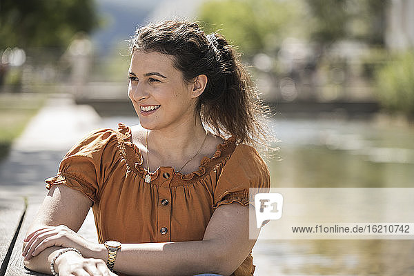 Smiling young woman looking away while sitting in park during sunny day