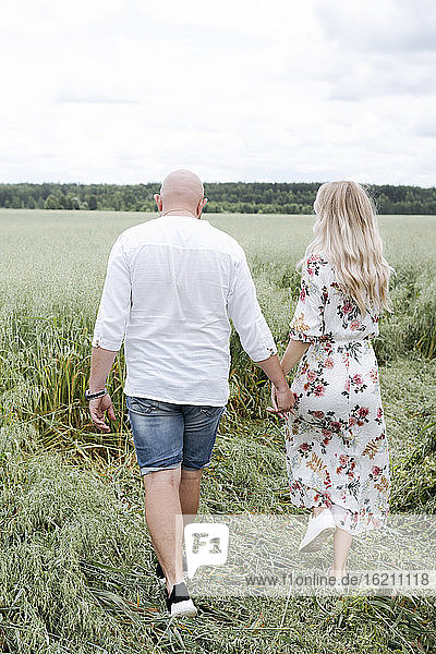 Couple holding hands while walking on oats field against sky