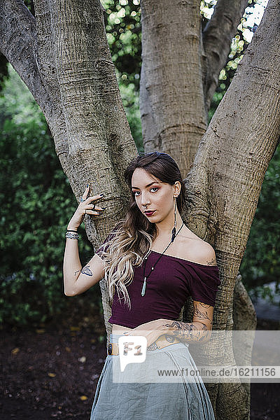 Porträt einer jungen Frau  die sich an einen Baum im Park lehnt