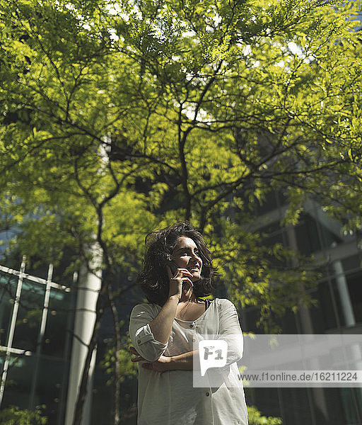Lächelnde junge Frau  die an einem Baum stehend mit ihrem Handy telefoniert