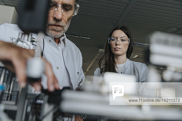 Männliche und weibliche Wissenschaftler mit Schutzbrillen bei der Untersuchung einer Maschine im Labor