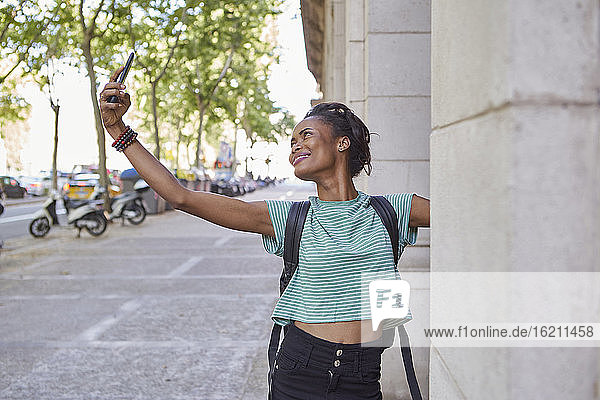 Glückliche junge Frau  die ein Selfie mit einer Säule auf dem Gehweg macht