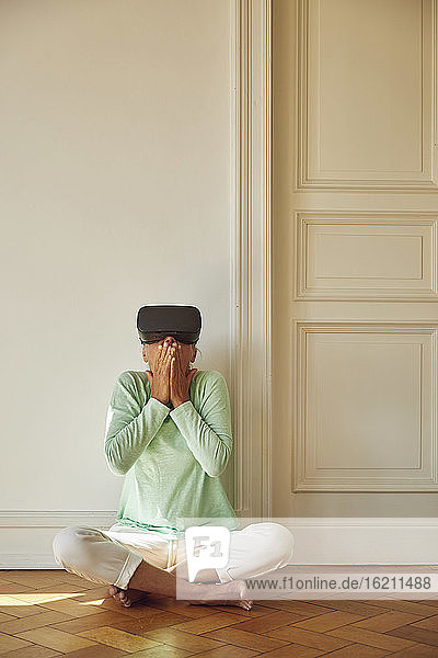 Ältere Frau benutzt einen Virtual-Reality-Simulator  während sie zu Hause auf dem Boden sitzt
