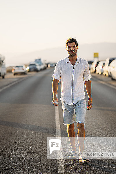Smiling mid adult man walking on road against clear sky during sunset