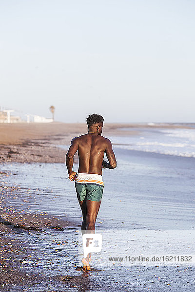 Hemdloser junger Mann läuft am Ufer gegen den klaren Himmel