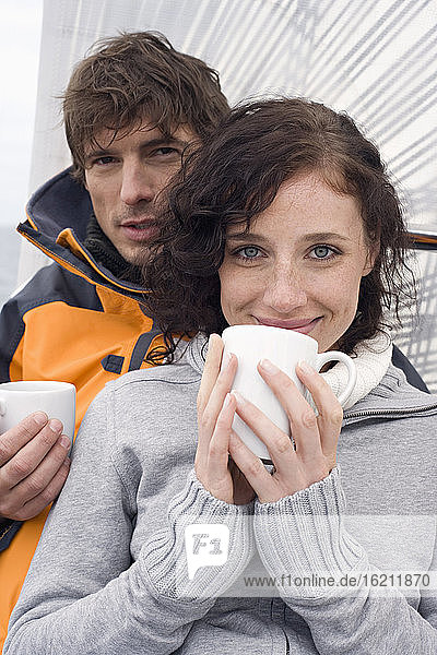 Germany  Baltic Sea  Lübecker Bucht  Young couple on sailing boat sitting and holding mugs  portrait