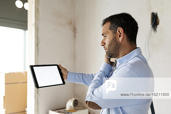 Architekt mit Tablet am Telefon in einem im Bau befindlichen Haus