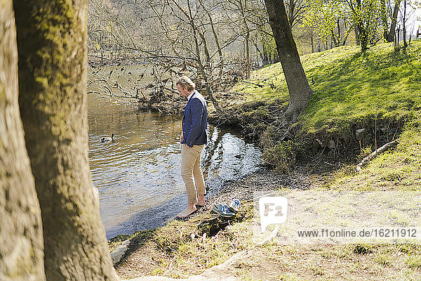Männlicher Unternehmer steht am Flussufer im Park an einem sonnigen Tag