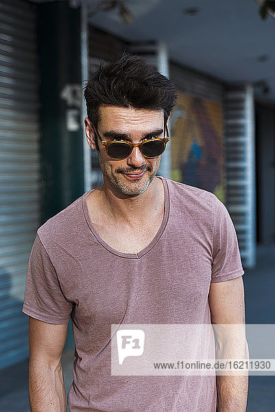 Gut aussehender Mann mit Sonnenbrille  der vor einem Gebäude steht