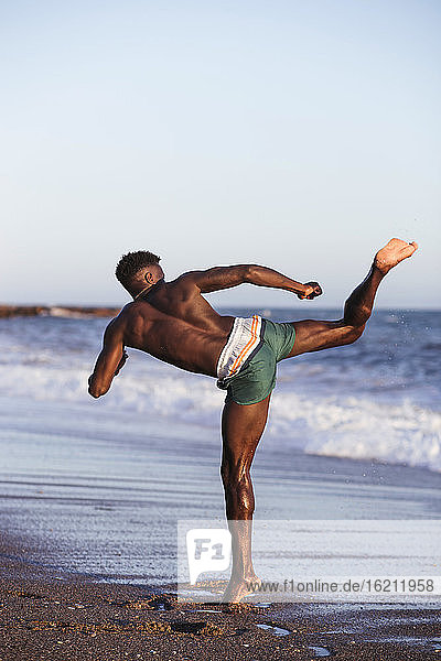 Shirtless African young man exercising at beach against clear sky