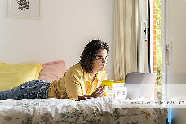 Frau mit Kreditkarte und Laptop im Schlafzimmer