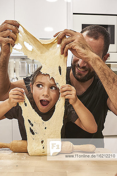 Vater und Tochter spielen mit Pizzateig auf einem Tisch in der Küche