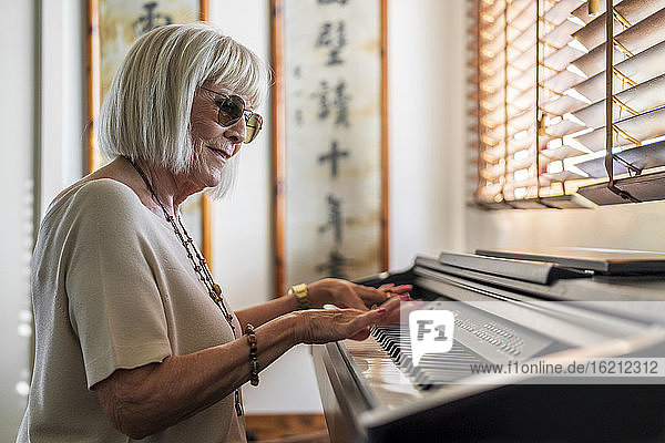 Ältere Frau mit Sonnenbrille spielt Klavier  während sie zu Hause sitzt