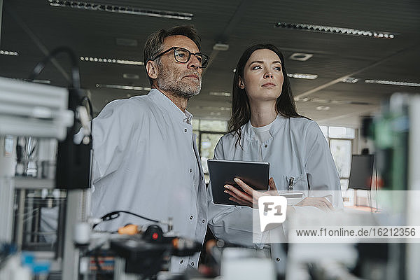 Thoughtful male and female engineers looking away while standing by machinery in laboratory