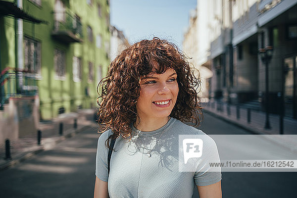Porträt einer lächelnden brünetten lockigen Frau in der Stadt