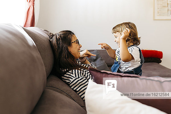 Happy mother and daughter talking while relaxing on sofa at home