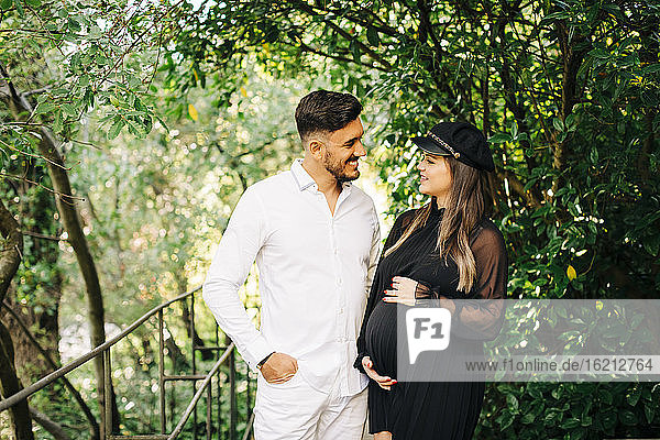 Lächelndes schwangeres Paar  das sich im Park stehend ansieht