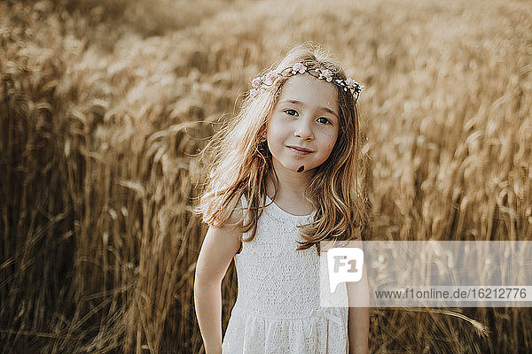 Cute blond girl standing in field of wheat
