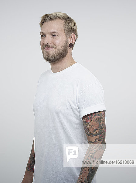 Junger Mann mit Tattoos vor weißem Hintergrund  lächelnd