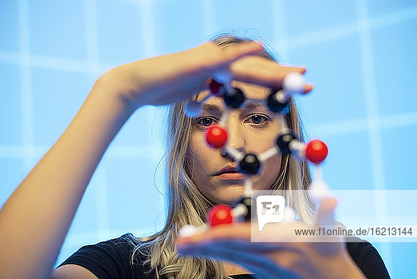 Nahaufnahme einer jungen Wissenschaftlerin  die ein Molekülmodell vor einem blauen Gittermuster hält