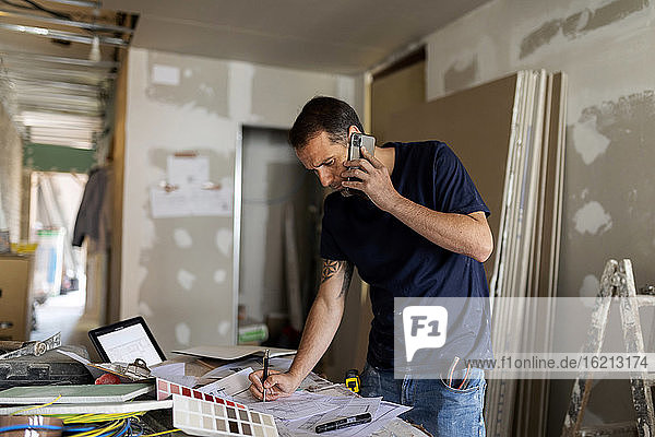 Mann am Telefon arbeitet an einem Bauplan