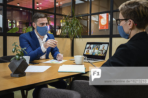 Männliche und weibliche Unternehmer tragen Masken bei der Strategieplanung im Sitzungssaal während einer Pandemie