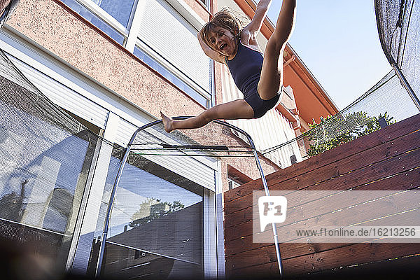 Verspieltes Mädchen springt auf Trampolin gegen Haus während sonnigen Tag