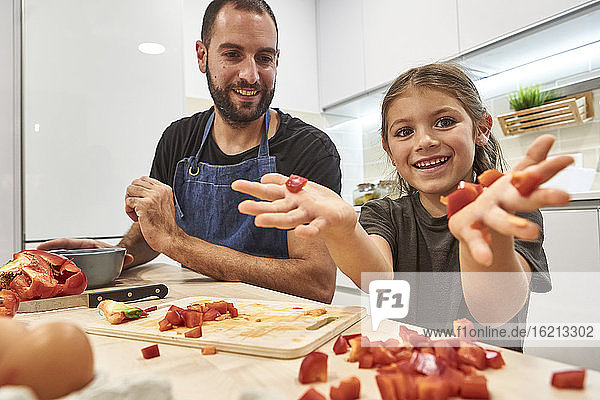 Glückliches Mädchen zeigt Paprikastücke  während es mit seinem Vater in der Küche sitzt