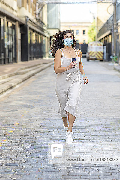 Junge Frau mit Maske läuft auf der Straße in der Stadt