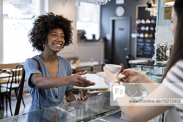 Happy woman taking coffee from owner in cafe