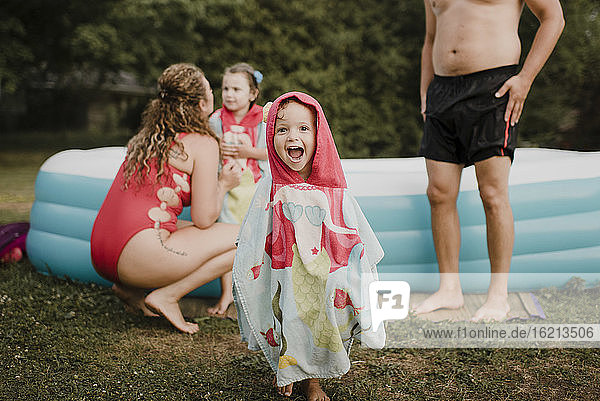 Glückliches Mädchen in einem lustigen Handtuch eingewickelt an einem aufblasbaren Schwimmbad im Garten