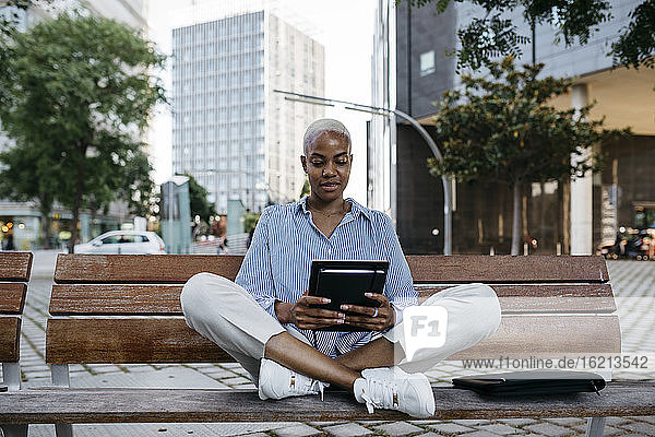 Geschäftsfrau mit digitalem Tablet auf einer Bank in der Stadt sitzend