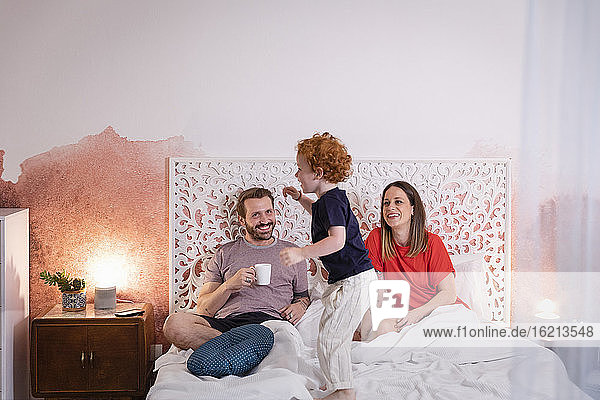 Parents looking at playful son while relaxing on bed