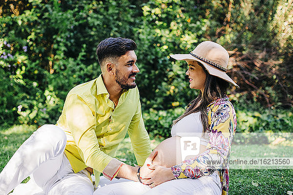 Lächelndes  erwartungsvolles Paar  das sich beim Sitzen im Park gegenseitig anschaut