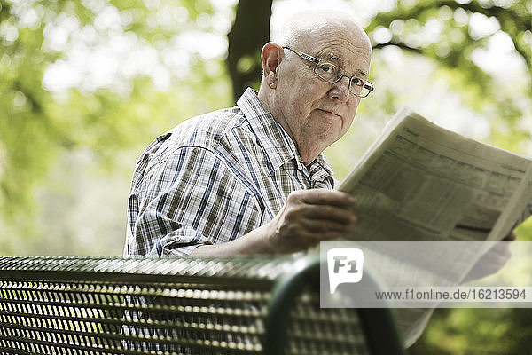 Deutschland  Nordrhein-Westfalen  Köln  Porträt eines älteren Mannes  der auf einer Bank im Park Zeitung liest