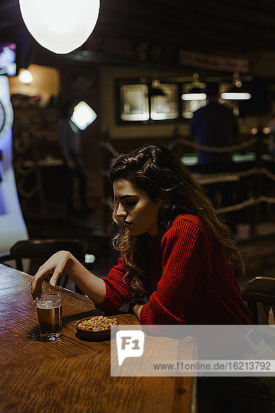 Traurige Mid Adult Frau mit Alkohol und Snacks auf dem Tisch sitzen im Restaurant