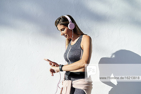 Smiling woman with headphones using phone while checking the time in city