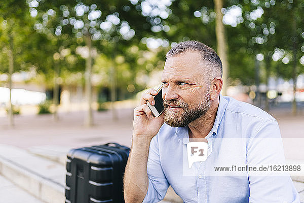 Geschäftsmann  der im Freien sitzend mit seinem Smartphone telefoniert